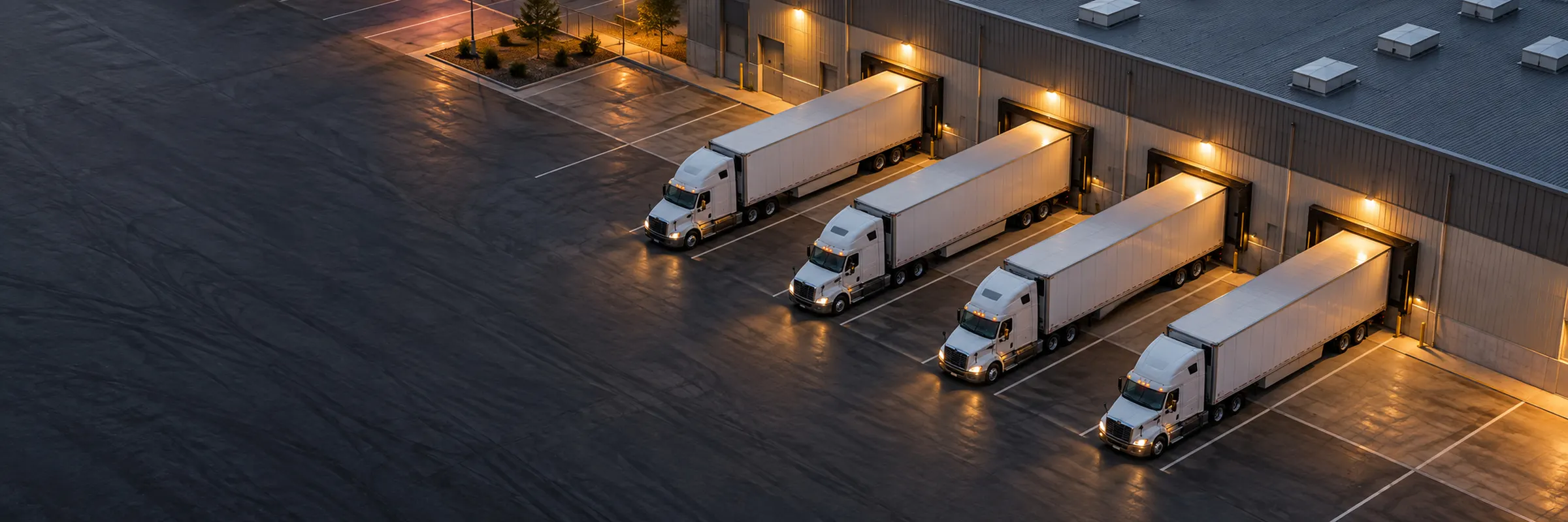 Four trucks backed onto lit loading docks at a warehouse at dusk
